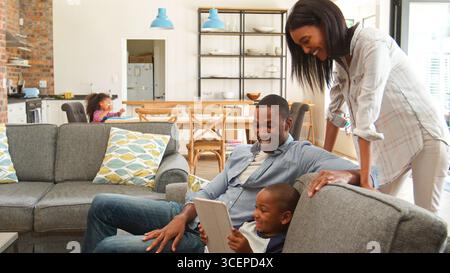 Sohn Zu Hause Sitzt Auf Sofa In Der Lounge Mit Eltern Mit Digitalem Tablet Stockfoto