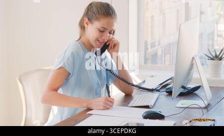 Junge Geschäftsfrau, Die Am Schreibtisch Am Computer Arbeitet Und Telefoniert Stockfoto