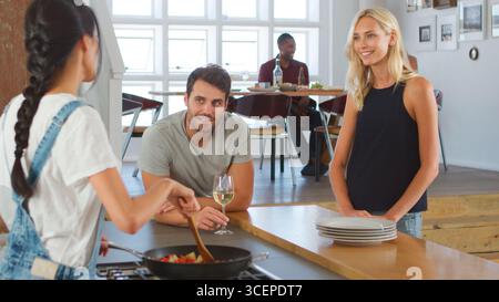 Frau, Die Mit Gästen Spricht, Während Sie Zu Hause In Moderner Küche Essen Für Dinner Party Macht Stockfoto