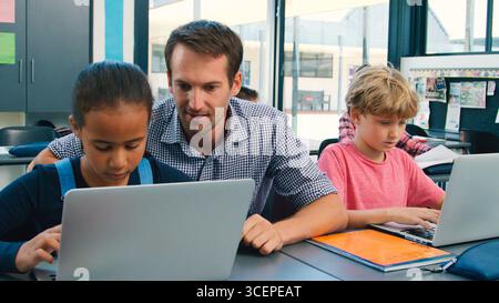 Männlicher Gymnasiallehrer Mit Schülern, Die Laptops Am Schreibtisch In Der Technikklasse Verwenden Stockfoto