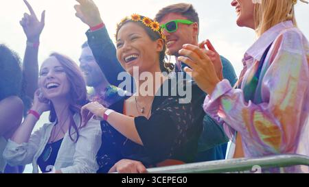 Junge Freunde im Publikum hinter Schranke Tanzen und Singen bei Outdoor Festival Musik genießen Stockfoto