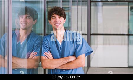 Porträt Der Lächelnden Männlichen Krankenschwester, Die Scrubs Trägt, Die Im Modernen Krankenhausgebäude Stehen Stockfoto