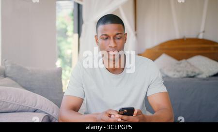 Mann, Der Zu Hause Im Schlafzimmer Sitzt Und Das Mobiltelefon Benutzt Stockfoto
