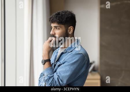 Ein nachdenklicher junger Geschäftsmann, der in der Entfernung im Fenster sitzt Stockfoto