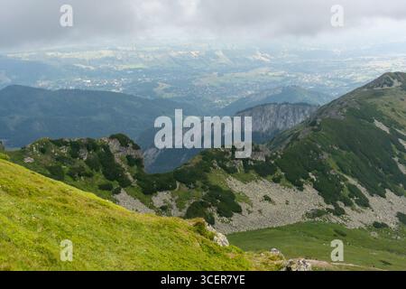Weitläufiger Blick auf die Bergkette mit geschichteten grünen Graten, die sich an trüben Tagen in weite Täler und Siedlungen erstrecken. Geografische Vielfalt, Berge Stockfoto