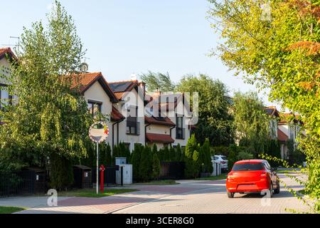Moderne Vorstadtstraße mit einer Reihe stilvoller Häuser mit roten Ziegeldächern, Solarpaneelen und grünen Bäumen an sonnigen Sommertagen. Umweltfreundliches Konzept Stockfoto
