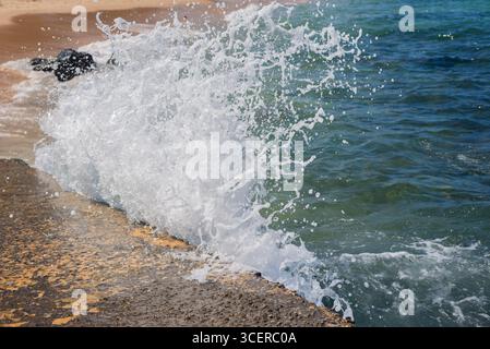 Spritzer einer Strandwelle, die hart gegen einen Zementpfeiler kracht. Wintersaison. Kraft der Natur. Stockfoto
