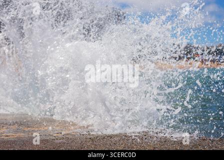 Spritzer einer Strandwelle, die hart gegen einen Zementpfeiler kracht. Wintersaison. Kraft der Natur. Stockfoto