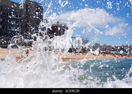 Spritzer einer Strandwelle, die hart gegen einen Zementpfeiler kracht. Wintersaison. Kraft der Natur. Stockfoto