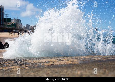 Spritzer einer Strandwelle, die hart gegen einen Zementpfeiler kracht. Wintersaison. Kraft der Natur. Stockfoto