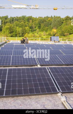Installation von Solarpaneelen auf einem Dach mit Bauarbeitern und Kran im Hintergrund, PV-Installation, gewerbliche Kunden, Neubau, Wiernshei Stockfoto