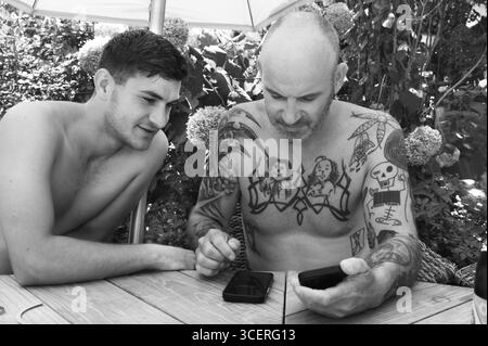 Vater und Sohn im Garten am Handy, Vater mit Tätowierungen auf Brust und Armen, Baden-Württemberg, Deutschland Stockfoto
