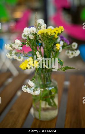 Rustikaler Blumenstrauß in Glasflasche mit Wasser auf Holztisch, im Freien in natürlicher Gartenumgebung. Rustikale Sommeratmosphäre, frisch Stockfoto