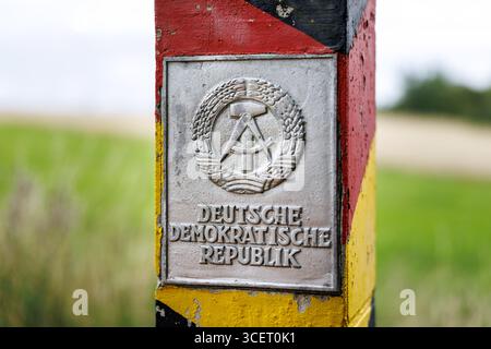 03. August 2025, Sachsen, Eichigt: Eine DDR-Grenzsäule (auch bekannt als Grenzposten, Grenzposten, DDR-Grenzposten, DDR-Grenzpfosten oder DDR-Grenzsäulen) in den Farben Schwarz, Rot und Gold mit einem Schild mit dem Staatswappen der DDR und der Aufschrift „Deutsche Demokratische Republik“ ist am 03.08.2025 an der ehemaligen innerdeutschen Grenze bei Eichigt im Vogtlandkreis in Sachsen bei Hof zu sehen. Die Staatsgrenzmarkierungen wurden erstmals im Herbst 1967 an der innerdeutschen Grenze errichtet. Zum Zeitpunkt der DDR das Gebiet, auf dem diese G Stockfoto