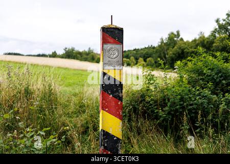 03. August 2025, Sachsen, Eichigt: Eine DDR-Grenzsäule (auch bekannt als Grenzposten, Grenzposten, DDR-Grenzposten, DDR-Grenzpfosten oder DDR-Grenzsäulen) in den Farben Schwarz, Rot und Gold mit einem Schild mit dem Staatswappen der DDR und der Aufschrift „Deutsche Demokratische Republik“ ist am 03.08.2025 an der ehemaligen innerdeutschen Grenze bei Eichigt im Vogtlandkreis in Sachsen bei Hof zu sehen. Die Staatsgrenzmarkierungen wurden erstmals im Herbst 1967 an der innerdeutschen Grenze errichtet. Zum Zeitpunkt der DDR das Gebiet, auf dem diese G Stockfoto