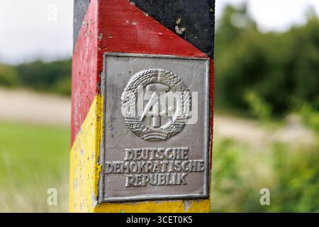 03. August 2025, Sachsen, Eichigt: Eine DDR-Grenzsäule (auch bekannt als Grenzposten, Grenzposten, DDR-Grenzposten, DDR-Grenzpfosten oder DDR-Grenzsäulen) in den Farben Schwarz, Rot und Gold mit einem Schild mit dem Staatswappen der DDR und der Aufschrift „Deutsche Demokratische Republik“ ist am 03.08.2025 an der ehemaligen innerdeutschen Grenze bei Eichigt im Vogtlandkreis in Sachsen bei Hof zu sehen. Die Staatsgrenzmarkierungen wurden erstmals im Herbst 1967 an der innerdeutschen Grenze errichtet. Zum Zeitpunkt der DDR das Gebiet, auf dem diese G Stockfoto
