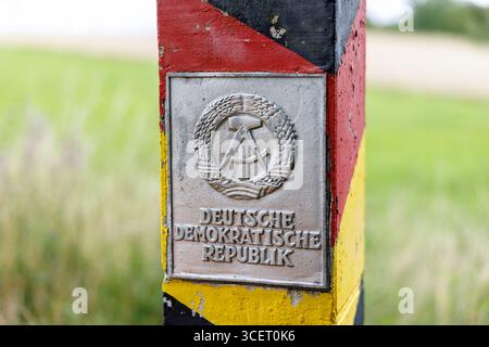 03. August 2025, Sachsen, Eichigt: Eine DDR-Grenzsäule (auch bekannt als Grenzposten, Grenzposten, DDR-Grenzposten, DDR-Grenzpfosten oder DDR-Grenzsäulen) in den Farben Schwarz, Rot und Gold mit einem Schild mit dem Staatswappen der DDR und der Aufschrift „Deutsche Demokratische Republik“ ist am 03.08.2025 an der ehemaligen innerdeutschen Grenze bei Eichigt im Vogtlandkreis in Sachsen bei Hof zu sehen. Die Staatsgrenzmarkierungen wurden erstmals im Herbst 1967 an der innerdeutschen Grenze errichtet. Zum Zeitpunkt der DDR das Gebiet, auf dem diese G Stockfoto