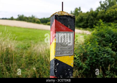 03. August 2025, Sachsen, Eichigt: Eine DDR-Grenzsäule (auch bekannt als Grenzposten, Grenzposten, DDR-Grenzposten, DDR-Grenzpfosten oder DDR-Grenzsäulen) in den Farben Schwarz, Rot und Gold mit einem Schild mit dem Staatswappen der DDR und der Aufschrift „Deutsche Demokratische Republik“ ist am 03.08.2025 an der ehemaligen innerdeutschen Grenze bei Eichigt im Vogtlandkreis in Sachsen bei Hof zu sehen. Die Staatsgrenzmarkierungen wurden erstmals im Herbst 1967 an der innerdeutschen Grenze errichtet. Zum Zeitpunkt der DDR das Gebiet, auf dem diese G Stockfoto