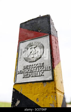 03. August 2025, Sachsen, Eichigt: Eine DDR-Grenzsäule (auch bekannt als Grenzposten, Grenzposten, DDR-Grenzposten, DDR-Grenzpfosten oder DDR-Grenzsäulen) in den Farben Schwarz, Rot und Gold mit einem Schild mit dem Staatswappen der DDR und der Aufschrift „Deutsche Demokratische Republik“ ist am 03.08.2025 an der ehemaligen innerdeutschen Grenze bei Eichigt im Vogtlandkreis in Sachsen bei Hof zu sehen. Die Staatsgrenzmarkierungen wurden erstmals im Herbst 1967 an der innerdeutschen Grenze errichtet. Zum Zeitpunkt der DDR das Gebiet, auf dem diese G Stockfoto