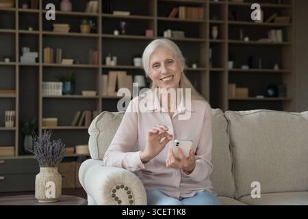 Heimporträt lächelnde pensionierte Dame, die sich mit dem Telefon auf der Couch entspannt Stockfoto