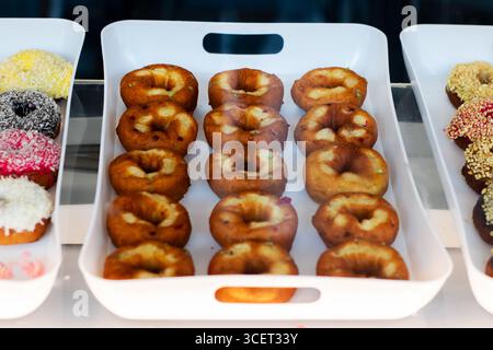Eine köstliche Auswahl an frisch gebackenen Donuts auf einem Tablett mit verschiedenen Belägen und Aromen, perfekt für jeden Liebhaber süßer Leckereien. Stockfoto