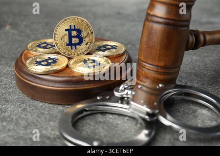 Kryptowährung. Bitcoins, Richtergabel und Handschellen auf grauem Tisch, Nahaufnahme Stockfoto