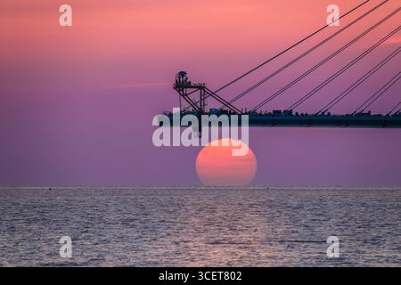 Wunderschöner Sonnenuntergang mit rosa und orangen Himmeln über der Danshui Tamsui Brücke im Bau in Taiwan, mit ruhigen Wellen. Erschossen am 29. April 2025. Stockfoto