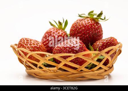 Ein Korb gefüllt mit frischen, Reifen Erdbeeren. Die Erdbeeren sind hellrot mit grünen Blättern, ordentlich in einem gewebten Korb angeordnet. Stockfoto
