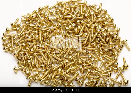 Ein Haufen goldener Schrauben, verstreut auf einer weißen Oberfläche. Die Schrauben sind klein, metallisch und haben eine glänzende Oberfläche, die für verschiedene Konstruktionen und geeignet ist Stockfoto