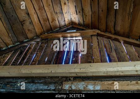 Nahaufnahme einer alten Holzdachwand mit verwitterten Dielen mit sichtbaren Lücken. Tageslicht strömt durch die Risse und offenbart die alte Textur Stockfoto
