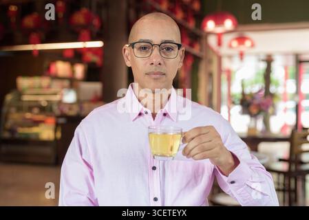 Glatze Hispanic reifer Mann in den 40er Jahren mit rosa lässigem Business-Shirt und Brille im chinesischen Teehaus-Restaurant. Kulturbegriff Relaxati Stockfoto