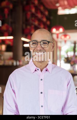 Glatze Hispanic reifer Mann in den 40er Jahren mit rosa lässigem Business-Shirt und Brille im chinesischen Teehaus-Restaurant. Kulturbegriff Relaxati Stockfoto