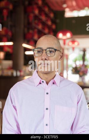 Glatze Hispanic reifer Mann in den 40er Jahren mit rosa lässigem Business-Shirt und Brille im chinesischen Teehaus-Restaurant. Kulturbegriff Relaxati Stockfoto