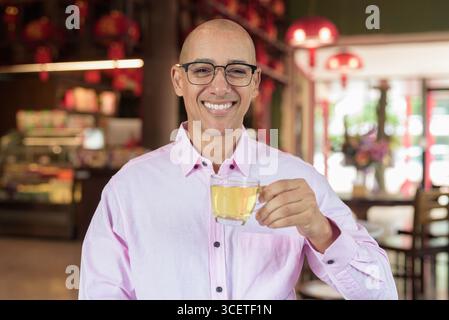 Glatze Hispanic reifer Mann in den 40er Jahren mit rosa lässigem Business-Shirt und Brille im chinesischen Teehaus-Restaurant. Kulturbegriff Relaxati Stockfoto
