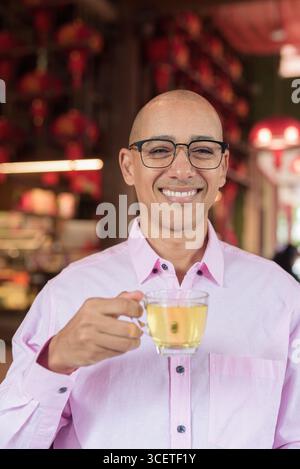 Glatze Hispanic reifer Mann in den 40er Jahren mit rosa lässigem Business-Shirt und Brille im chinesischen Teehaus-Restaurant. Kulturbegriff Relaxati Stockfoto