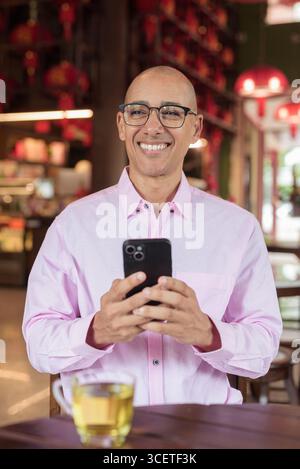 Glatze Hispanic reifer Mann in den 40er Jahren mit rosa lässigem Business-Shirt und Brille im chinesischen Teehaus-Restaurant. Kulturbegriff Relaxati Stockfoto
