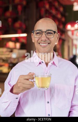 Glatze Hispanic reifer Mann in den 40er Jahren mit rosa lässigem Business-Shirt und Brille im chinesischen Teehaus-Restaurant. Kulturbegriff Relaxati Stockfoto