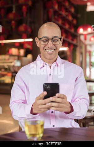 Glatze Hispanic reifer Mann in den 40er Jahren mit rosa lässigem Business-Shirt und Brille im chinesischen Teehaus-Restaurant. Kulturbegriff Relaxati Stockfoto