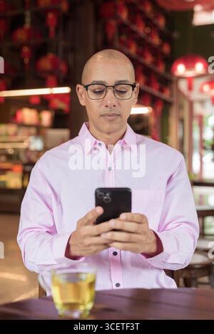 Glatze Hispanic reifer Mann in den 40er Jahren mit rosa lässigem Business-Shirt und Brille im chinesischen Teehaus-Restaurant. Kulturbegriff Relaxati Stockfoto