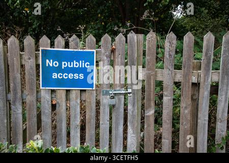 Kein öffentliches Zutrittsschild an einem verschlossenen Holztor und Zaun mit Bäumen und Büschen dahinter. Zutrittsbeschränkung, privates Grundstückskonzept in ländlicher Umgebung. Stockfoto