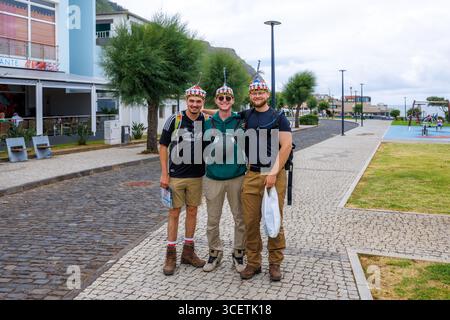 Porto Moniz, Madeira, Portugal – 7. Juli 2025; drei glückliche, lächelnde Freunde mit traditionellen Madeira-Mützen posieren auf einer Straße in Porto Moniz. Hoch qua Stockfoto