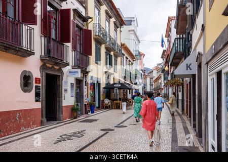 Funchal, Portugal – 8. Juli 2025; schmale Fußgängerzone der Altstadt, in der Touristen schlendern. Fensterläden öffnen. Hochwertige Fotos Stockfoto