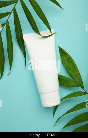 Weißes Kosmetikröhrchen mit grünen Blättern auf blauem Hintergrund. Mockup für das Branding von Kosmetikprodukten. Stockfoto
