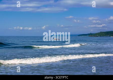 Malerischer Blick auf eine ruhige Küste mit sanften Meereswellen, ein Fischerboot am Horizont unter klarem Himmel. Golden Hour Shot Stockfoto