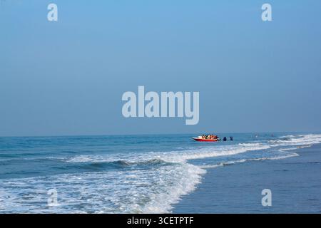 Malerischer Blick auf eine ruhige Küste mit sanften Meereswellen, ein Fischerboot am Horizont unter klarem Himmel. Golden Hour Shot Stockfoto