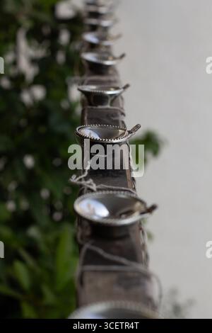 Eine Reihe von kleinen metallischen Öllampen ist in einer Linie auf einer Schiene angeordnet, deren Hintergrund unscharf grün ist, was auf Grün im Freien hindeutet Stockfoto