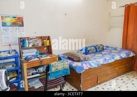 Kompakter Schreibtisch mit Büchern und wichtigen Dingen neben einem Holzbett in einem kleinen Schlafzimmer Stockfoto