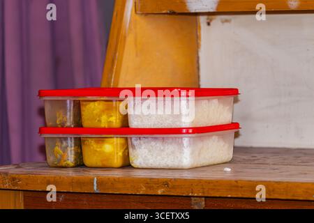 Frisch gepackte hausgemachte Mahlzeit für das Hostel mit Reis und Curry in Plastikkisten mit rotem Deckel auf Holztisch Stockfoto