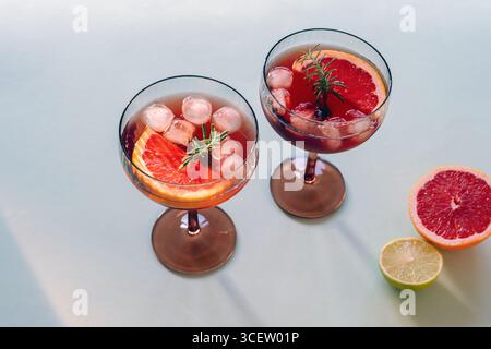 Zwei Cocktailgläser mit Grapefruitscheiben, Eiswürfeln und Rosmarin auf hellem Hintergrund. Erfrischende Sommergetränke. Stockfoto