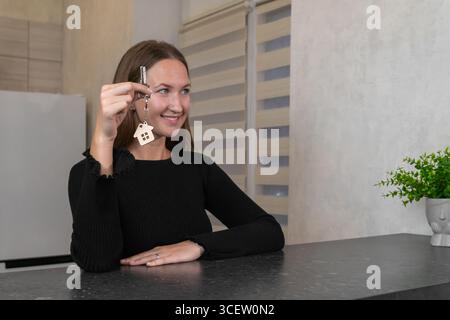 Lächelnde Frau, die Schlüssel mit Schlüsselanhänger zeigt. Wir feiern den Immobilienkauf. Immobilieninvestitionen. Neues Wohneigentum. Genehmigung von Hypothekarkrediten. S Stockfoto